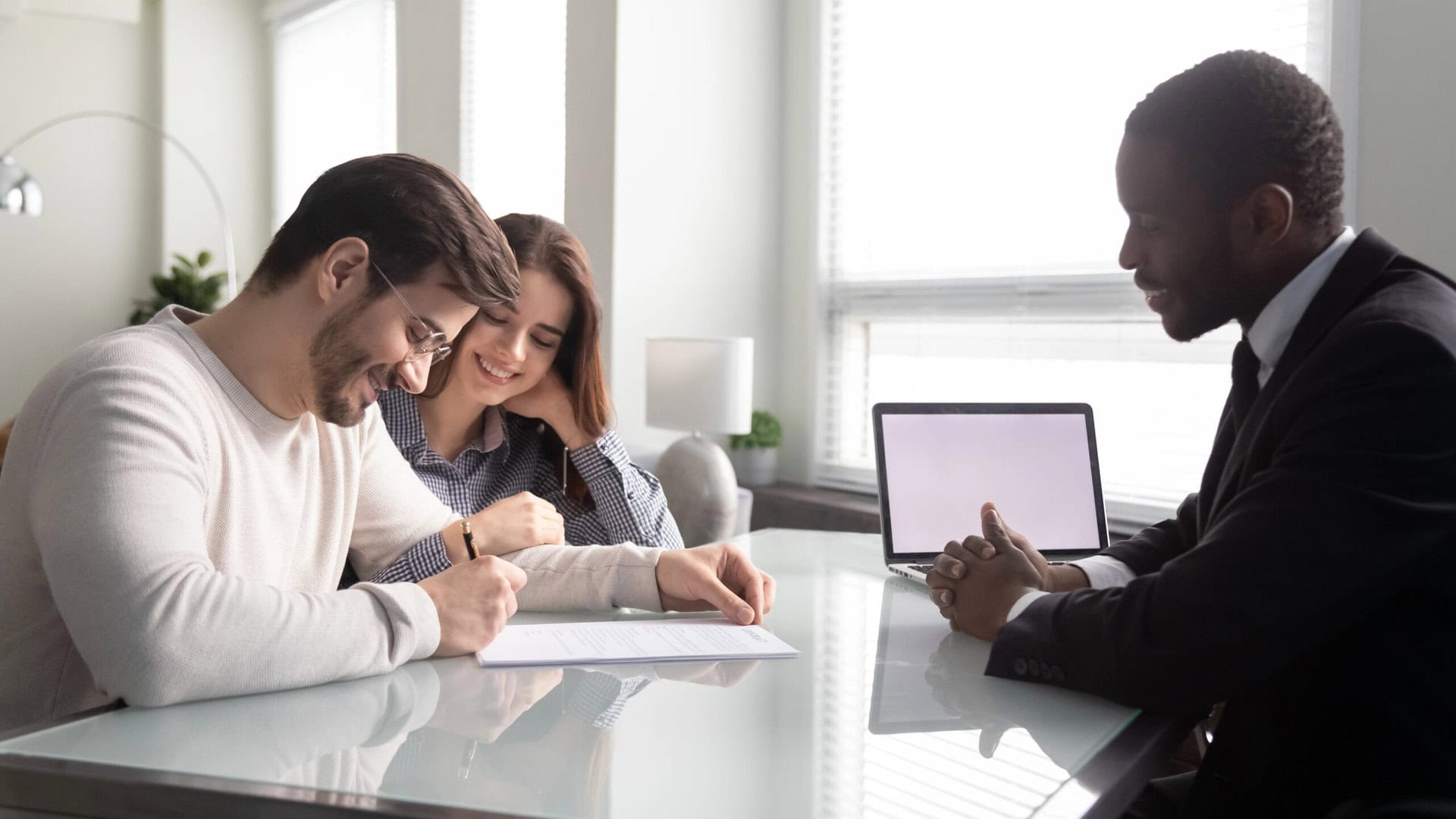 Side view happy young family couple signing contract, satisfied with first big purchase, glad to receive bank credit loan mortgage. Smiling african american insurer meeting with positive clients.